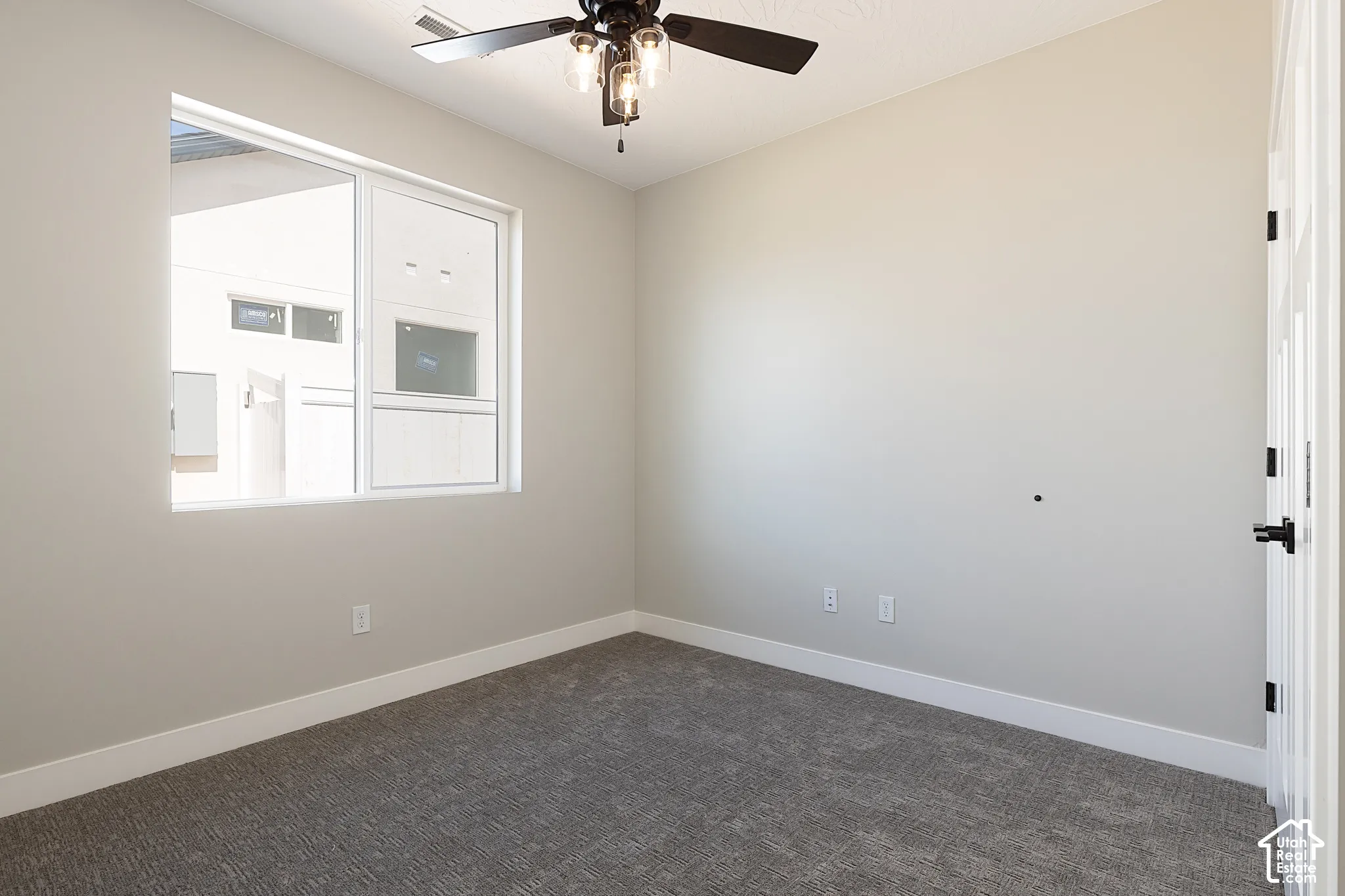 Room featuring neutral wall paint, wall-to-wall carpeting, a large sliding window, and a ceiling fan with integrated glass-shade lighting