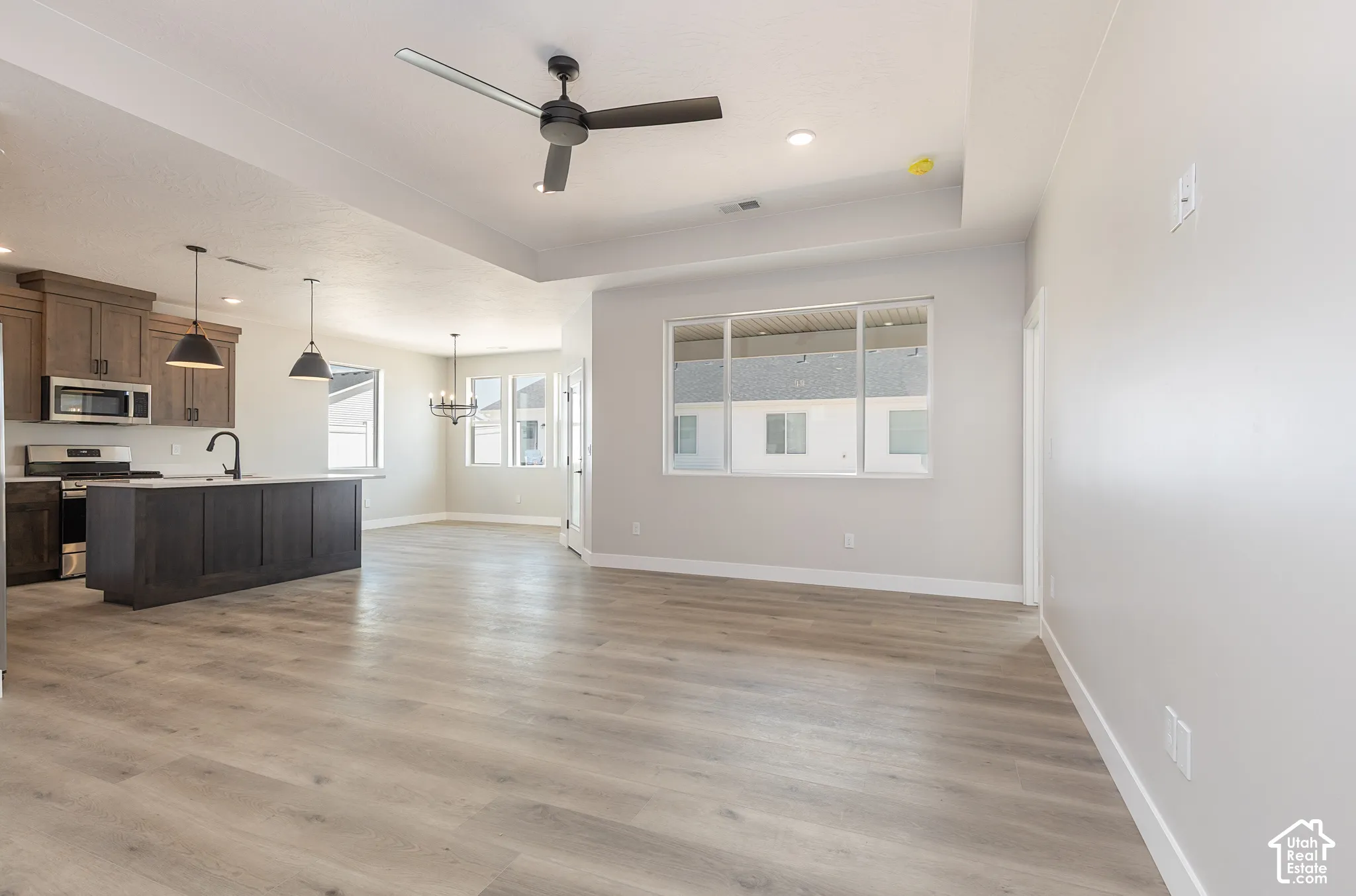 Open-concept interior featuring wood-finish flooring, tray ceilings, recessed lighting, and a kitchen equipped with a central island and dark-toned cabinetry