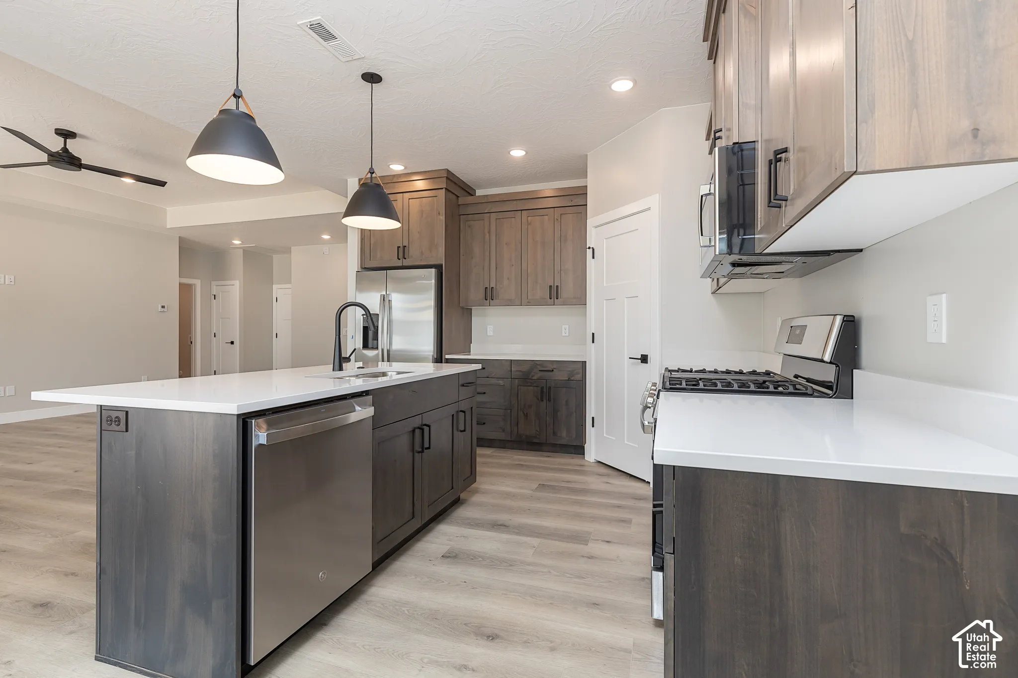 Kitchen featuring stained wood cabinetry, stone-finish countertops, stainless steel appliances, a central island with a matte black faucet, and wood-finish flooring