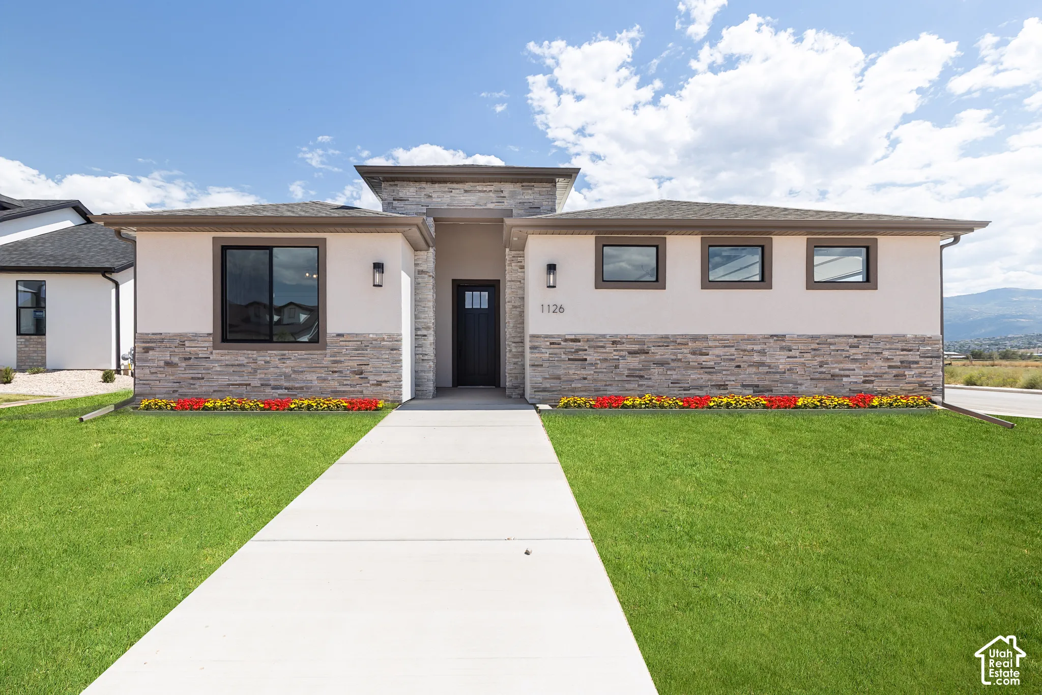 Single-story exterior featuring light-toned stucco, multi-textured stone veneer, concrete walkway, and black-trimmed horizontal windows
