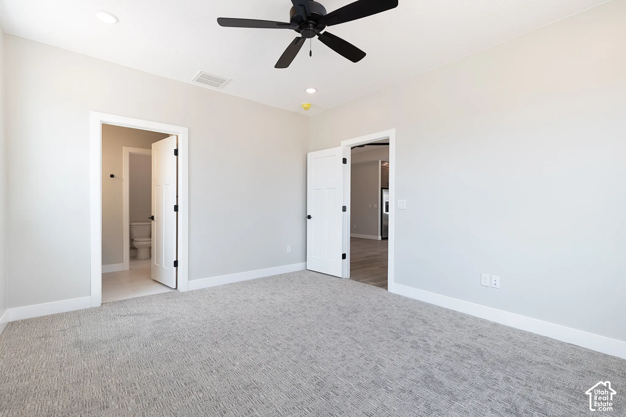 Neutral-toned interior space featuring textured carpeting, a matte black ceiling fan, recessed lighting, and white interior doors with black hardware