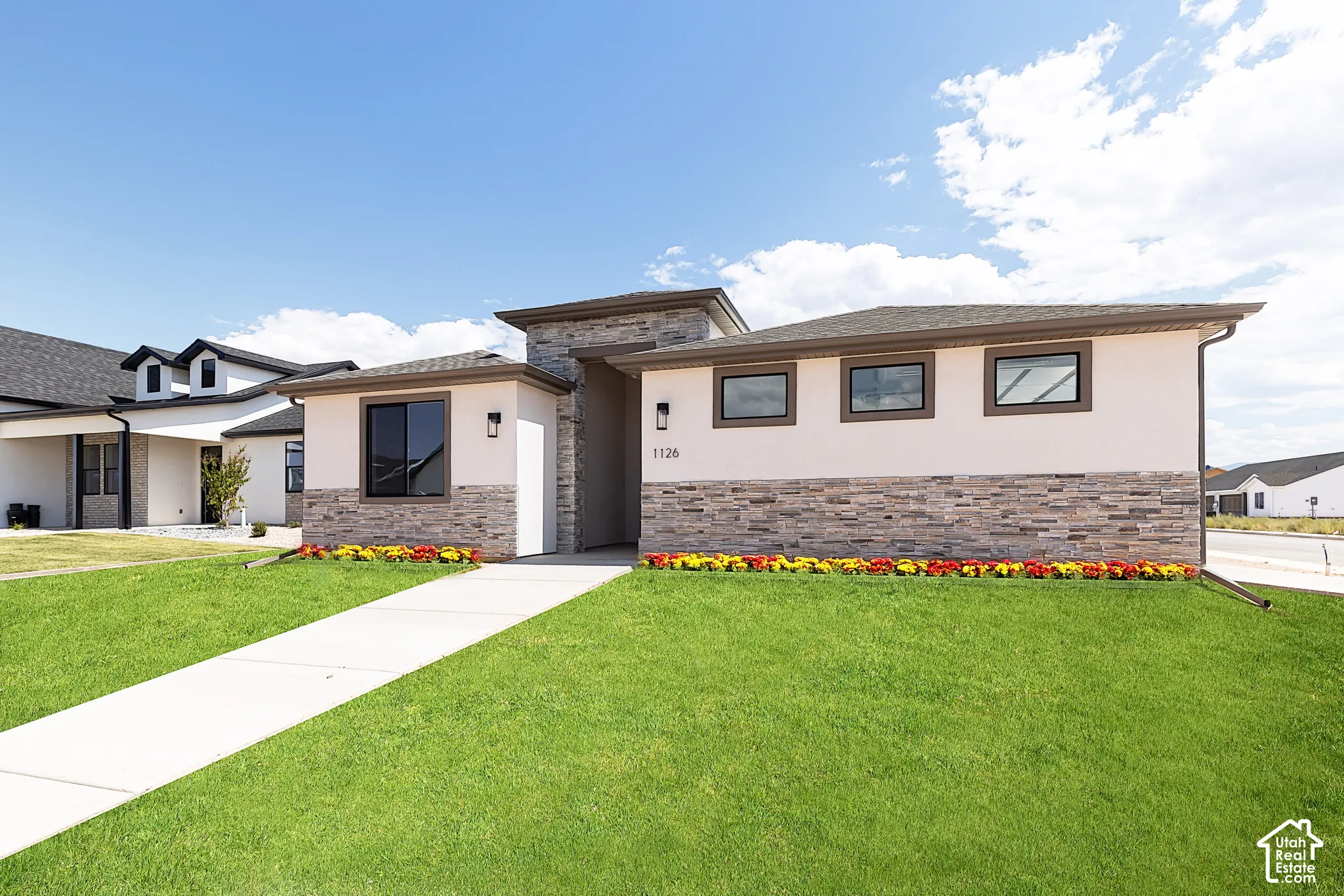 Contemporary exterior featuring a stucco finish, stone veneer accents, a concrete walkway, and low-profile rectangular windows