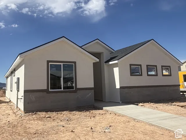 Single-story residence featuring a dual-tone stucco exterior, a composition shingle roof, dark-trimmed window frames, and a concrete walkway