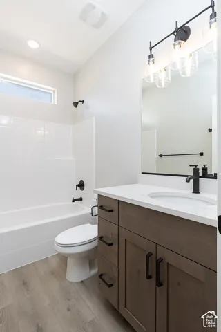 Bathroom featuring a wooden vanity with matte black hardware, stone-composite countertop, white tile-surround tub, wood-finish flooring, and industrial-style multi-light fixture