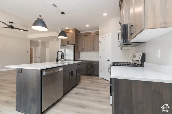 Kitchen featuring stained wood cabinetry, stone-finish countertops, stainless steel appliances, a central island with a matte black faucet, and wood-finish flooring