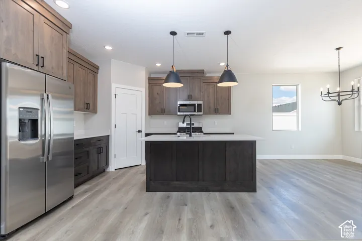 Kitchen featuring wood-finish cabinetry, a contrasting center island with a stone-surface countertop, stainless steel appliances, matte black hardware, and wood-finish flooring
