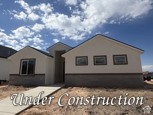 Exterior facade featuring a neutral-toned stucco finish, a covered entryway, dual-pitched rooflines, dark window trim, and a concrete walkway