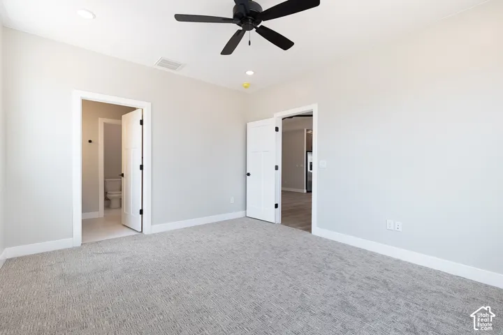 Neutral-toned interior space featuring textured carpeting, a matte black ceiling fan, recessed lighting, and white interior doors with black hardware