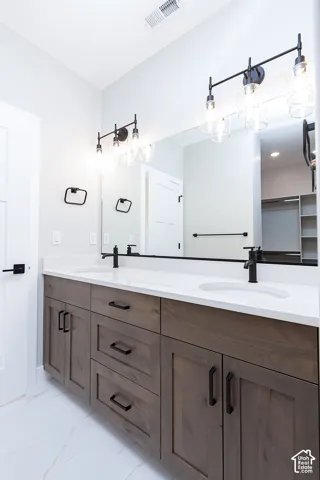 Dual-sink vanity featuring stained wood cabinetry, white stone-composite countertop, matte black hardware, and two multi-light vanity fixtures
