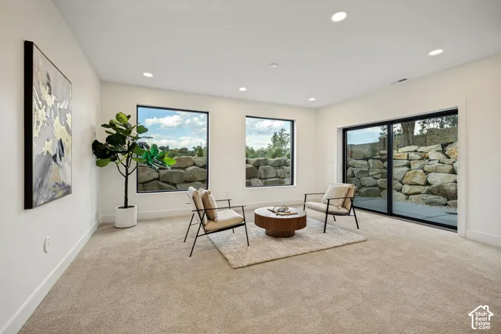 Neutral-toned wall-to-wall carpeting, recessed ceiling lighting, large picture windows with black frames, and expansive sliding glass doors featuring exterior boulder rock wall scenery