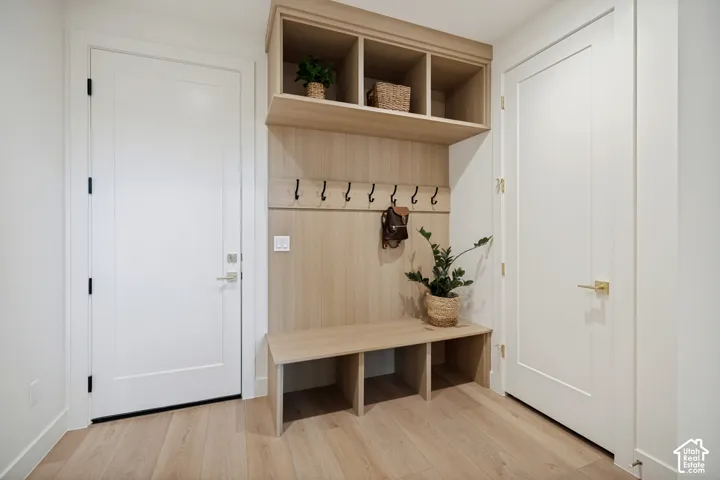 Built-in wood-finish mudroom cabinetry with an integrated bench, open overhead storage, and matte black wall-mounted hooks, complemented by wood-finish flooring and solid-core interior doors with metallic hardware
