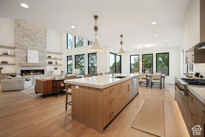 Open-concept kitchen and living area featuring high ceilings, wood-finish flooring, a floor-to-ceiling stone-faced fireplace, custom built-in shelving, and a large center island with quartz countertops