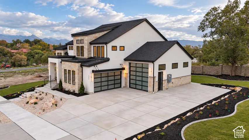 Contemporary exterior featuring smooth stucco finish, natural stone cladding, asphalt shingle roofing, dual glass-paneled garage doors, and a concrete driveway