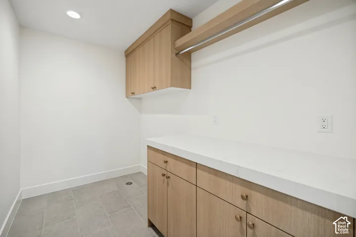 Light wood-finish cabinetry, quartz countertops, integrated hanging rod, and neutral ceramic floor tile