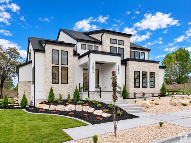 Multi-level contemporary exterior featuring smooth stucco finish, natural stone facade, dark window frames, and multi-pitched roofline