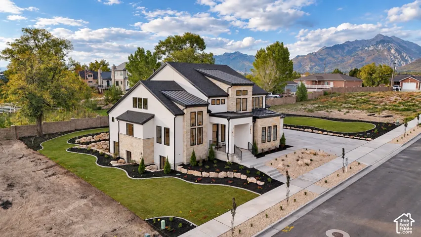Two-story residence featuring a mixed-material exterior of stone masonry and smooth siding, a metal roof, an attached concrete driveway, and professional landscaping set against a mountain backdrop