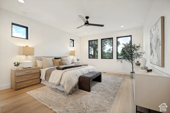 Bright room featuring light wood-finish flooring, recessed lighting, matte black ceiling fan, and large windows with black frames