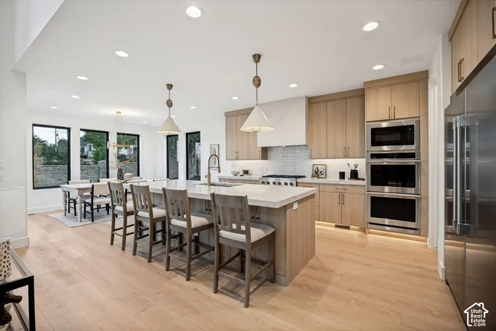 Kitchen featuring wood-finish cabinetry, a large central island with stone countertop, stainless steel double wall ovens, recessed lighting, and expansive windows with black frames