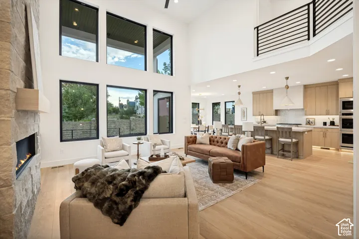 Double-height ceilings with expansive windows, stone-surround fireplace, wood-finish flooring, recessed lighting, and kitchen with large center island and built-in wall ovens