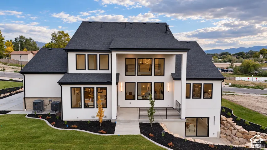 Contemporary two-story exterior featuring white stucco finish, high-contrast black window frames, steep-pitched gable roof, covered patio, and tiered stone retaining wall