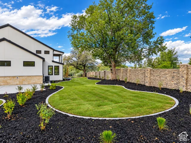 Landscaped backyard featuring a contoured lawn, dark mulch garden beds, stone perimeter wall, and mature trees
