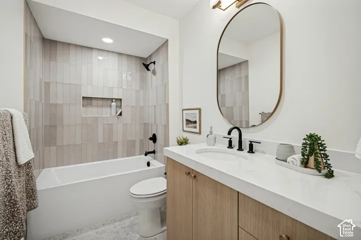 Bathroom featuring a wood-finish vanity with a stone-surface countertop, an oval wall-mounted mirror, a tub-shower combination with vertical tile surrounds, and matte black plumbing fixtures