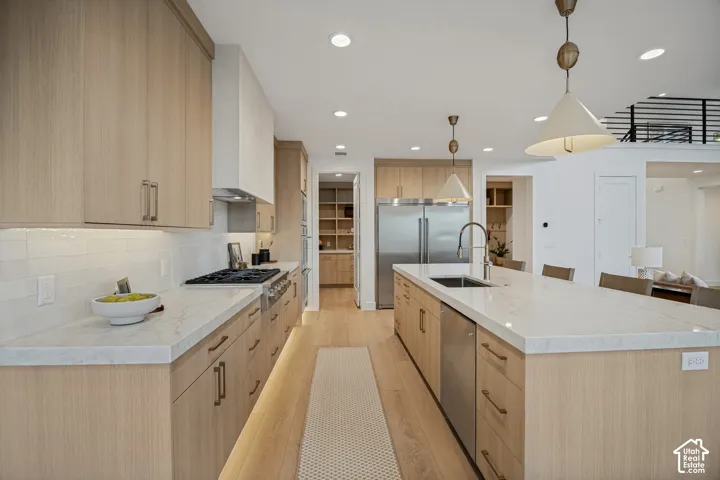 Kitchen featuring wood-finish cabinetry, stone-surface countertops, stainless steel appliances, a center island with an integrated sink, and recessed lighting
