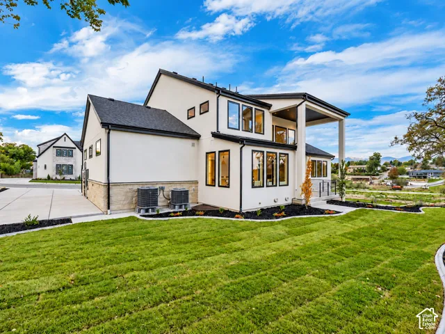 Contemporary two-story exterior featuring smooth stucco siding, stone veneer accents, dark-framed windows, a covered patio, and a concrete driveway