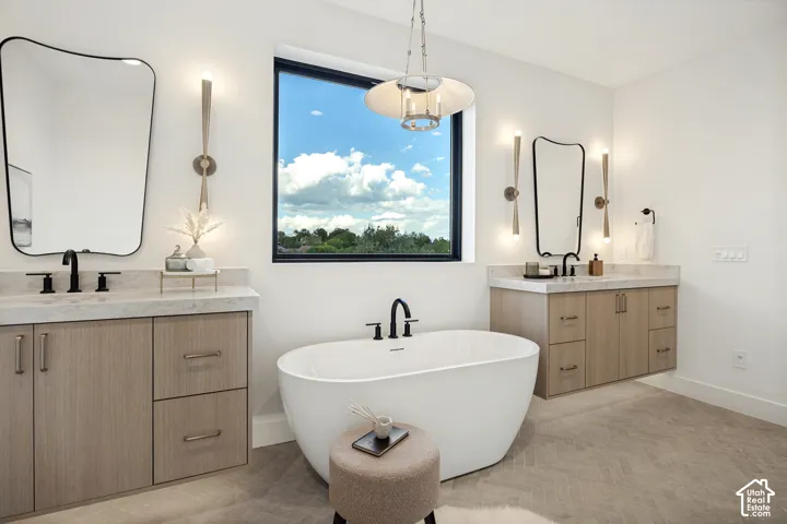 Dual wood-finish vanities with light-toned stone countertops, a freestanding soaking tub with matte black fixtures, and herringbone-patterned flooring