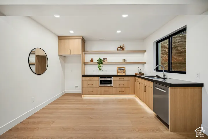 Kitchenette featuring light wood-finish cabinetry, dark solid-surface countertops, recessed under-cabinet lighting, dual floating shelves, and wood-finish flooring