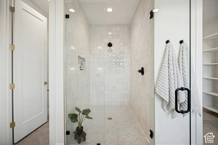 Walk-in shower featuring a glass enclosure, matte black fixtures, recessed shower niche, and tiled walls with a stone-finish floor
