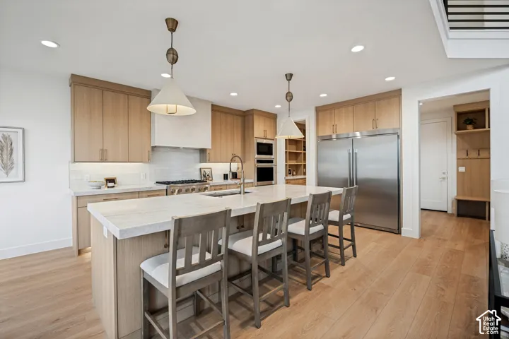 Kitchen featuring light wood-finish cabinetry, an oversized central island with stone-finish countertops, stainless steel dual-refrigerator, recessed lighting, and suspended pendant fixtures