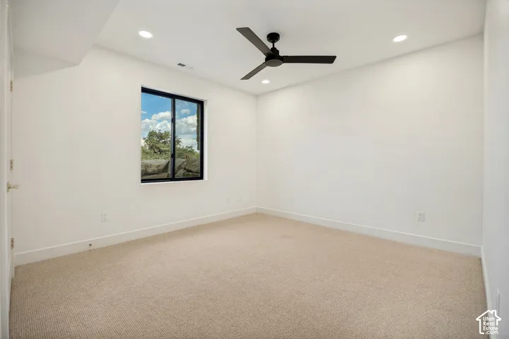 Neutral-toned carpeted flooring, recessed lighting, matte black ceiling fan, and a single-pane window with exterior rock landscaping