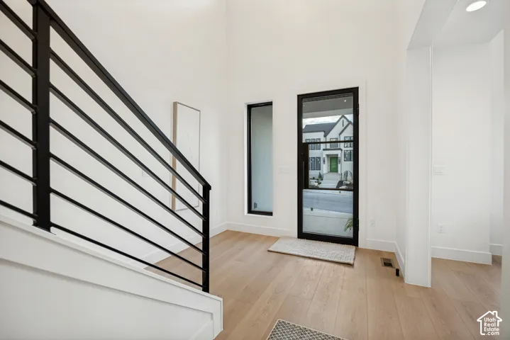 High-ceiling entryway featuring light-toned wood-finish flooring, a black metal-framed glass front door, and a staircase with black horizontal railings