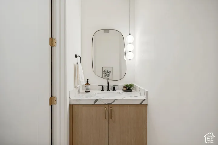 Wood-finish cabinetry vanity with stone-patterned countertop, integrated sink, matte black widespread faucet, organic-shaped wall mirror, and tiered spherical pendant lighting