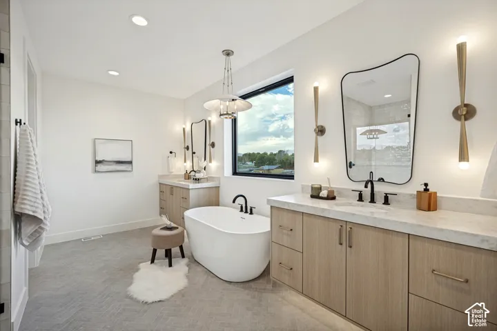 Bathroom featuring a freestanding soaking tub, dual wood-finish cabinetry with stone countertops, herringbone-patterned tile flooring, matte black fixtures, and custom wall-mounted lighting