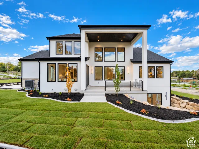 Modern exterior featuring clean white stucco siding, expansive picture windows, a covered patio with recessed lighting, black metal railing, and professional landscaping with stone hardscaping