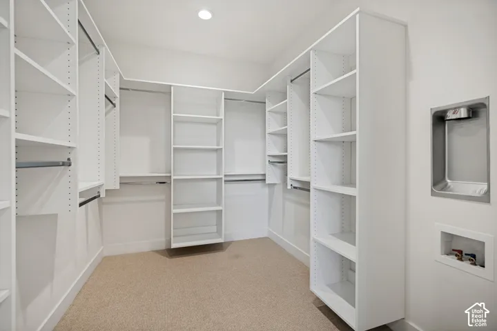 Walk-in storage space featuring built-in white shelving, integrated hanging rods, wall-to-wall carpeting, and recessed ceiling lighting