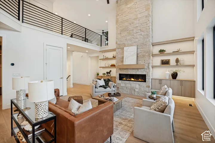 Two-story living area featuring a full-height stone fireplace with a linear insert, custom wood shelving with base cabinetry, light-toned wood-finish flooring, and a metal railing mezzanine