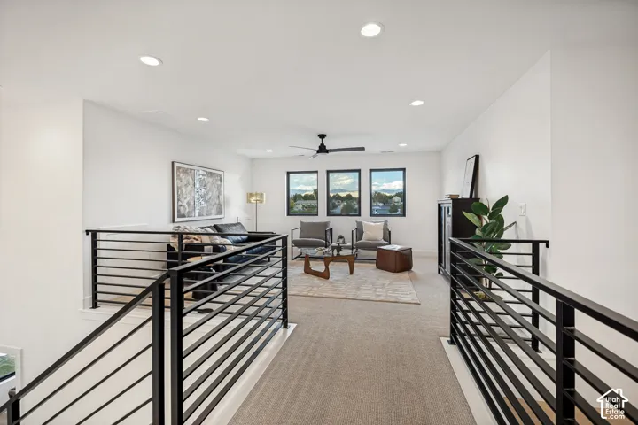 Open loft area featuring neutral carpeting, matte black horizontal-rail metal balustrades, recessed lighting, a modern ceiling fan, and large windows with dark frames