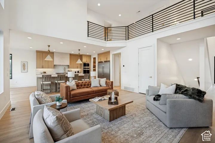Double-height ceiling, open-concept kitchen with wood-finish cabinetry, built-in stainless steel appliances, and a black metal horizontal-bar railing overlooking the floor below