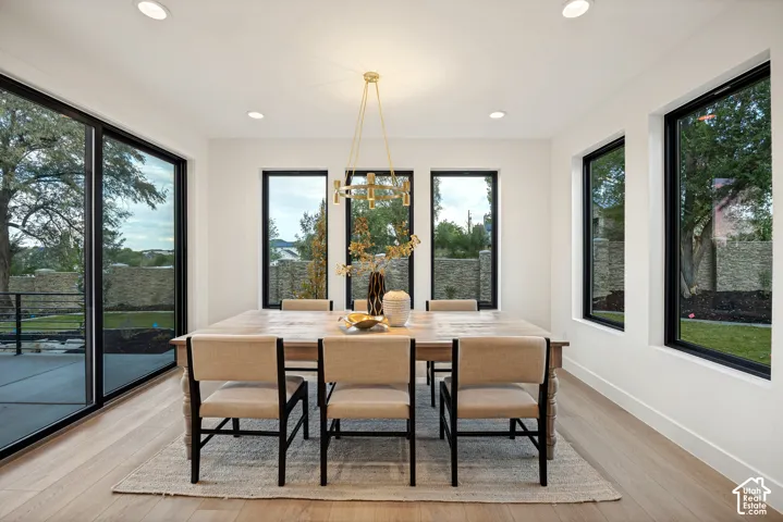 Dining area featuring wood-finish flooring, oversized windows with black frames, recessed lighting, and a multi-arm brass chandelier
