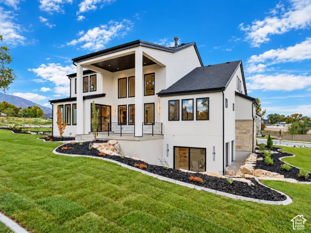 Contemporary two-story exterior featuring smooth stucco siding, stone veneer accents, multi-pane windows with black frames, a covered elevated deck, and a walk-out lower level