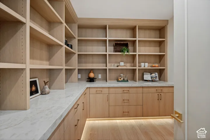 Built-in light-tone wood cabinetry featuring adjustable shelving, integrated under-cabinet lighting, natural stone countertops, and minimalist metal hardware