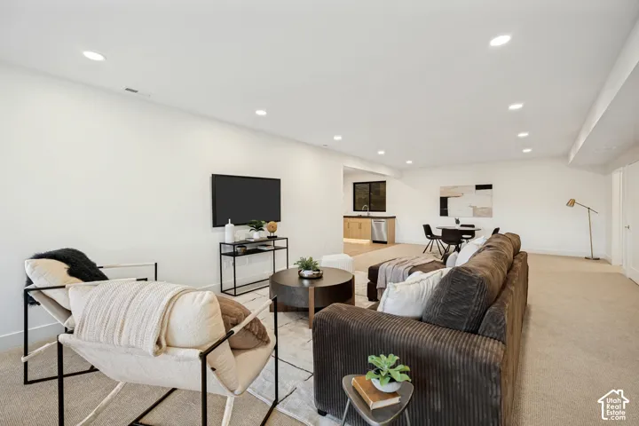 Open-concept area featuring neutral wall-to-wall carpeting, recessed ceiling lighting, and a wet bar equipped with stone-finish countertops and a stainless steel under-mount sink