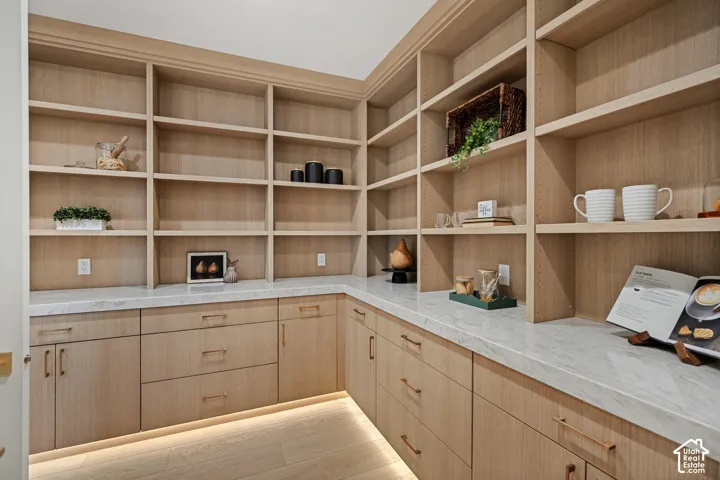 Custom cabinetry featuring light-toned wood finish, expansive stone-surface countertops, integrated under-cabinet lighting, and extensive floor-to-ceiling built-in shelving