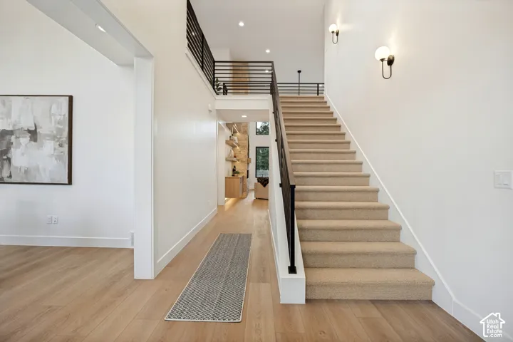 Foyer featuring wood-finish flooring, a staircase with carpeted treads, a matte black metal railing, and wall-mounted globe lighting