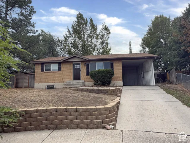 Brick exterior with a covered carport, concrete driveway, and a retaining wall