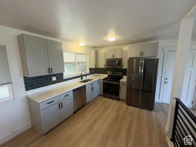 Kitchen featuring light-toned cabinetry, light countertops, dark subway tile backsplash, wood-finish flooring, and stainless steel appliances