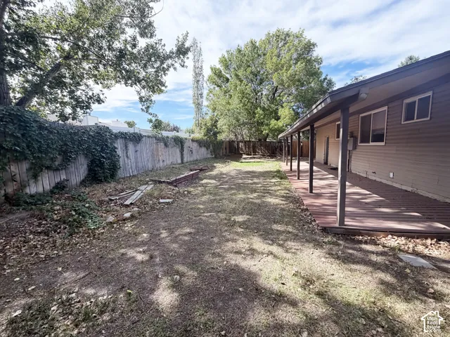 Expansive backyard featuring a covered patio with rich wood-finish decking, vertical siding, and a wooden fence with mature vine coverage